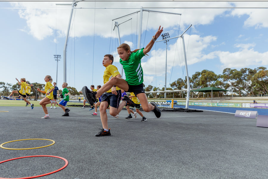 Children playing sports on a track with hula hoops and sports equipment.