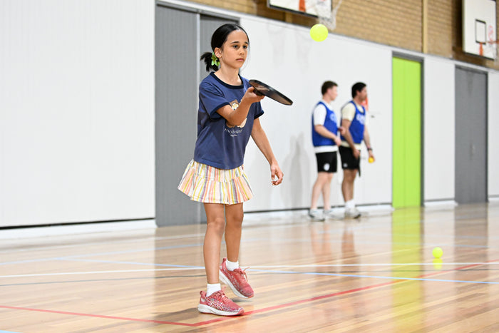Young girl full of concentration as she prepares to accept a pickleball at an ASC pickleball camp