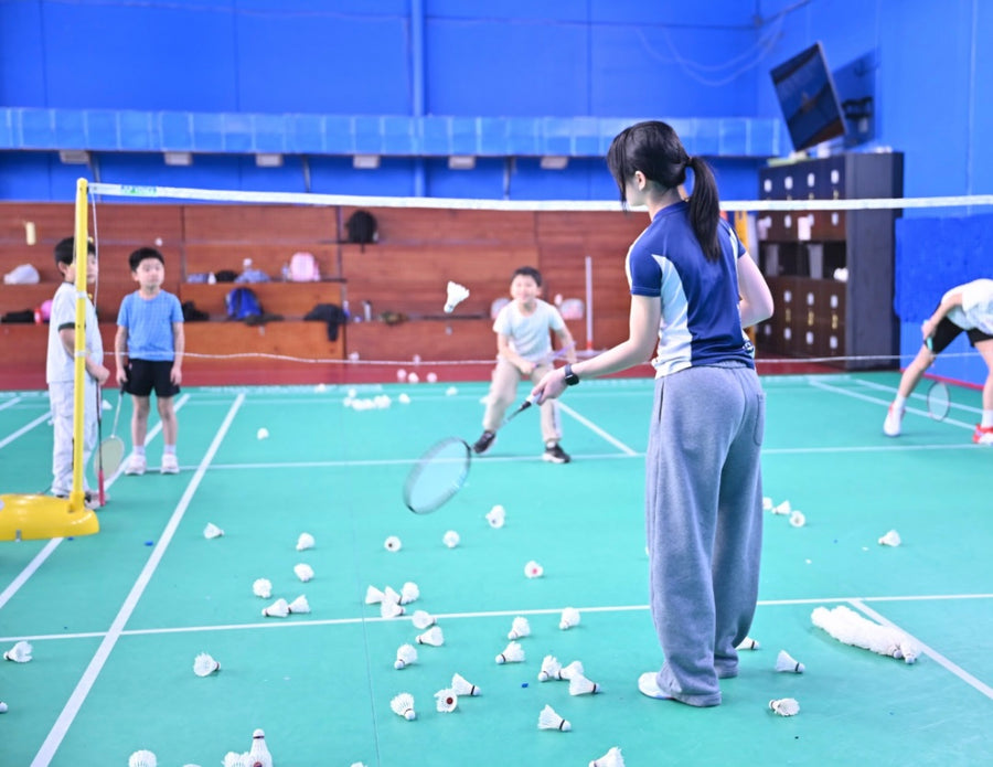 Badminton coach sending practice shuttlecock shots to an eager participant at an ASC badminton camp