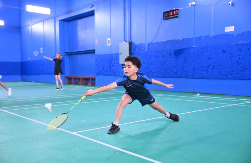 Young boy reaching at full extension to return a shuttlecock at an ASC badminton camp.