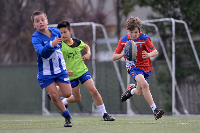 Three children playing a game of AFL at an ASC camp
