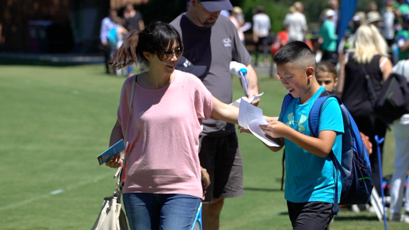 Mum collecting a happy boy who is delighted with his hand written coaches report at the end of an ASC Camp