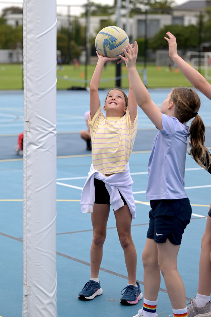 Two girls, one shooting the other waiting for a rebound at an ASC Netball Camp
