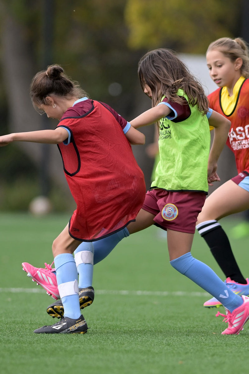 Three young female soccer players competing for the ball at an ASC socer camp