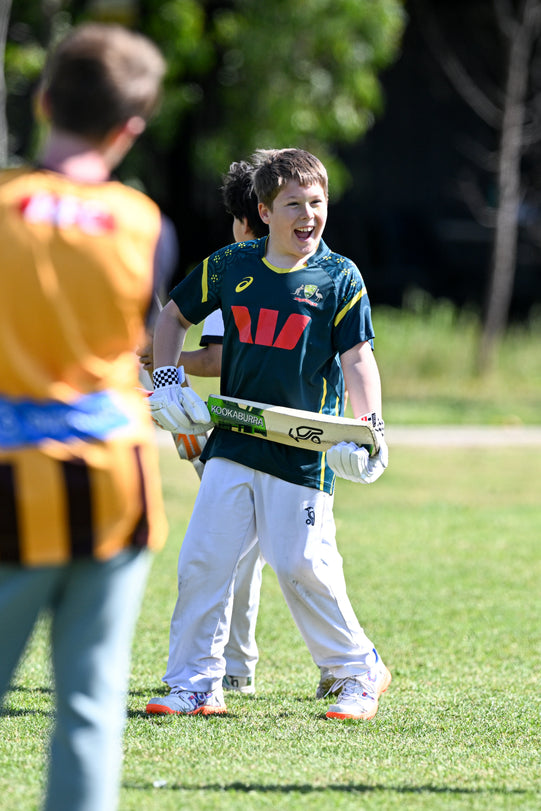 A young boy smiling while holding a cricket bat at an ASC cricket camp.