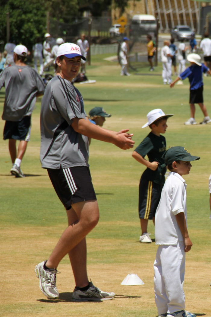 Coach at an ASC cricket camp giving instruction to young players on fielding skills