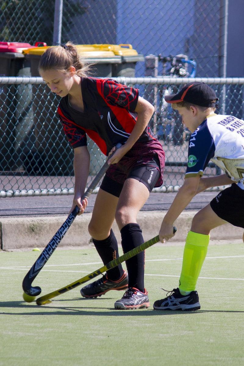 Young girl and boy competing for the ball during an ASC field hockey camp