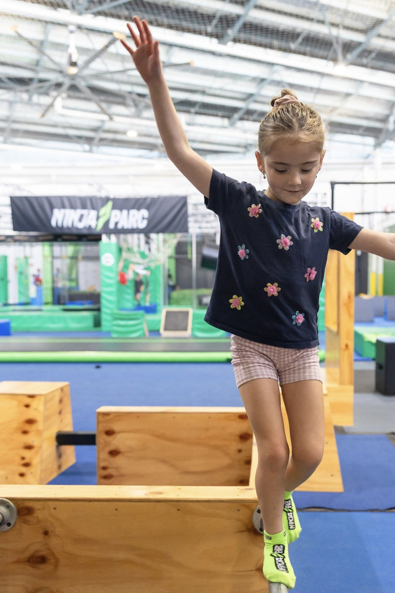 A young girl full of concentration as she walks across a balance rail at an indoor obstacle course at an ASC Nija Parc parkour skills program