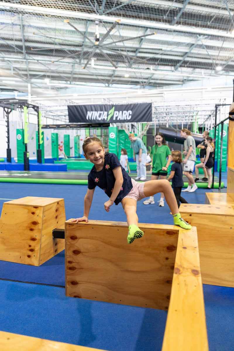 A happy young girl navigating an indoor obstacle course at an ASC Nija Parc parkour skills program