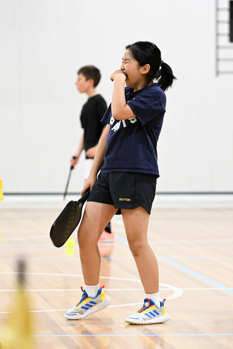 A young girl playing pickleball and having a wonderful time at an ASC pickleball training camp.