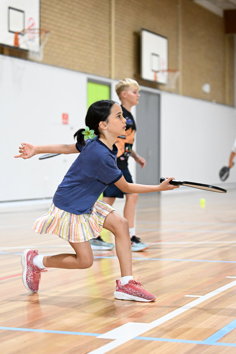 A girl in a dynamic lunge position, ready to receive a shot, at an ASC pickleball camp.