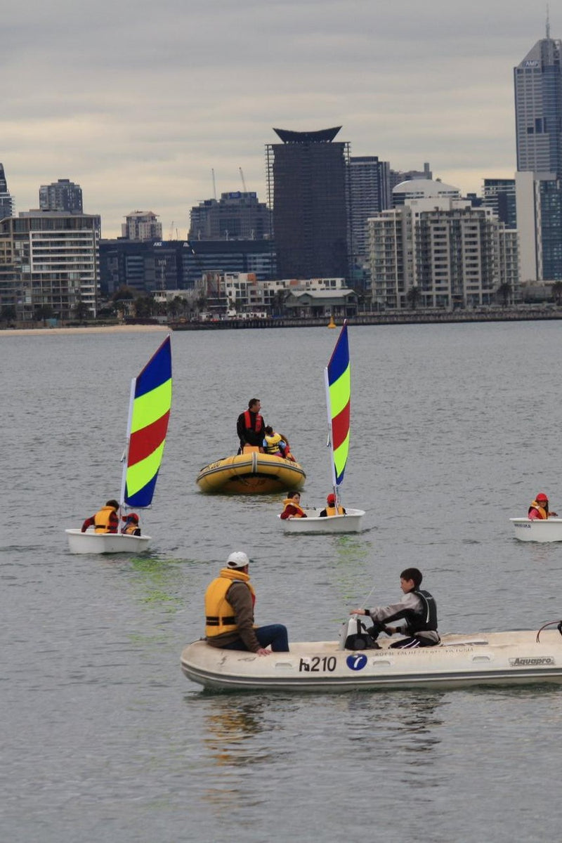 Kids sailing under the watchful eyes of two saling instructors out on the water with them. A great skyline backdrop for the ASC sailing coaching program.