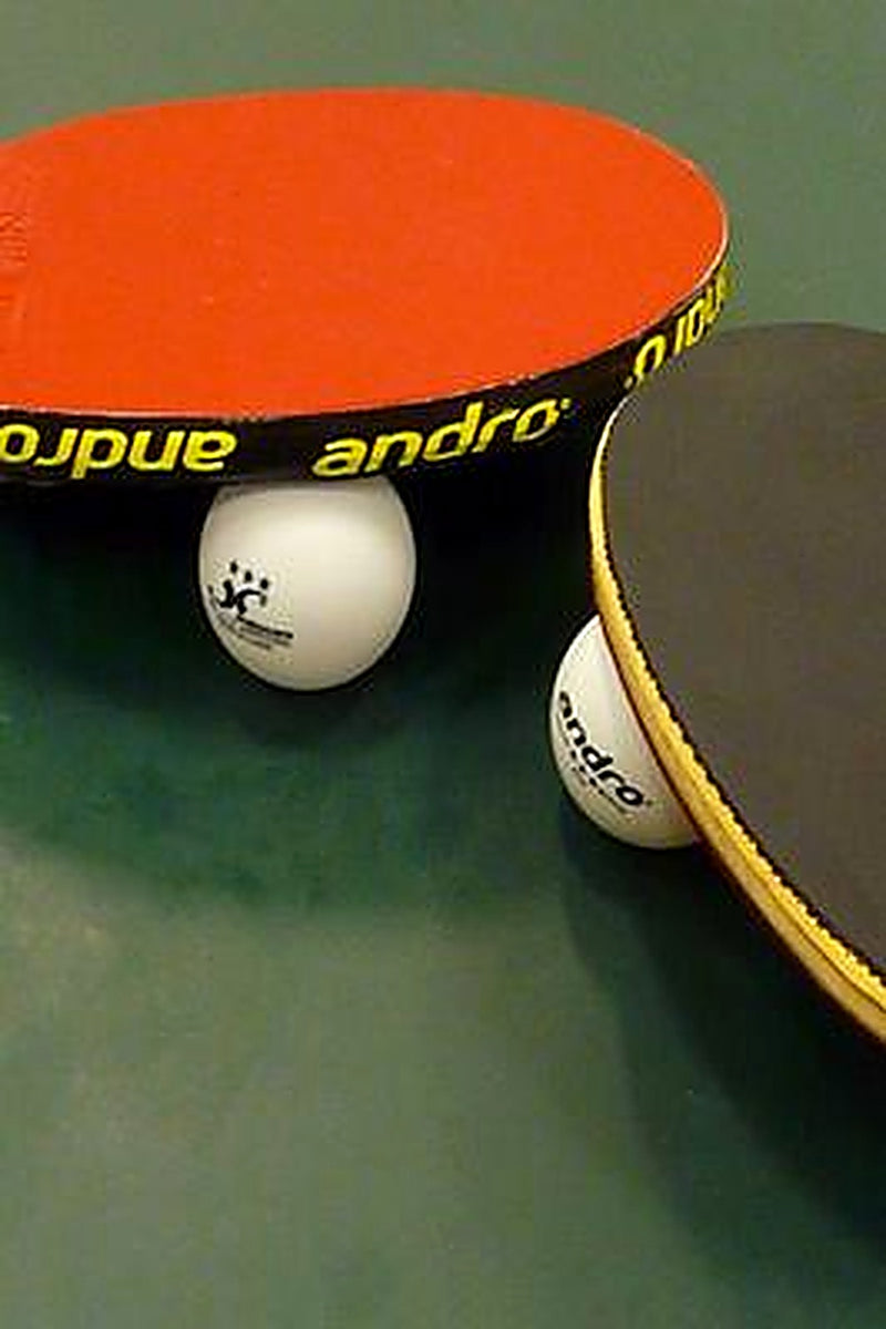 Two table tennis paddles and two white table tennis balls on a green table tennis table.
