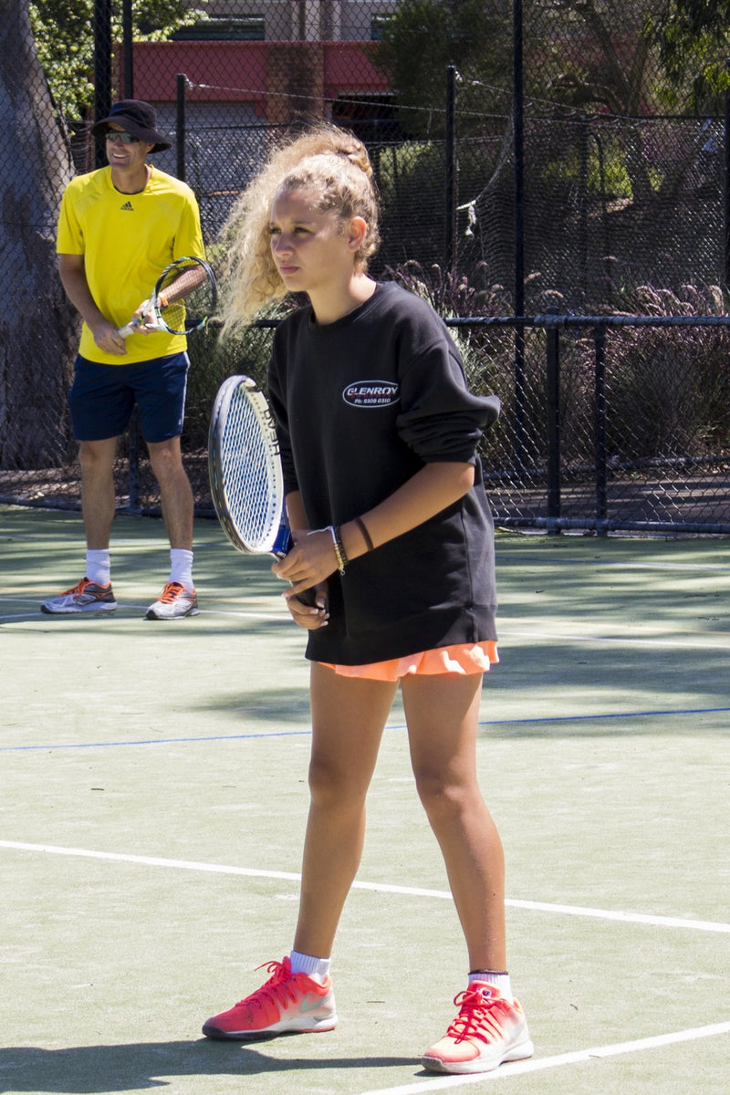 Young girl waiting to receive serve at an ASC tennis camp. Coach is in the background instructing on the next court