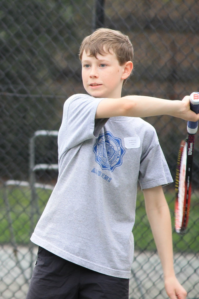 A young boy, mid-swing with a tennis racket, at an ASC tennis camp