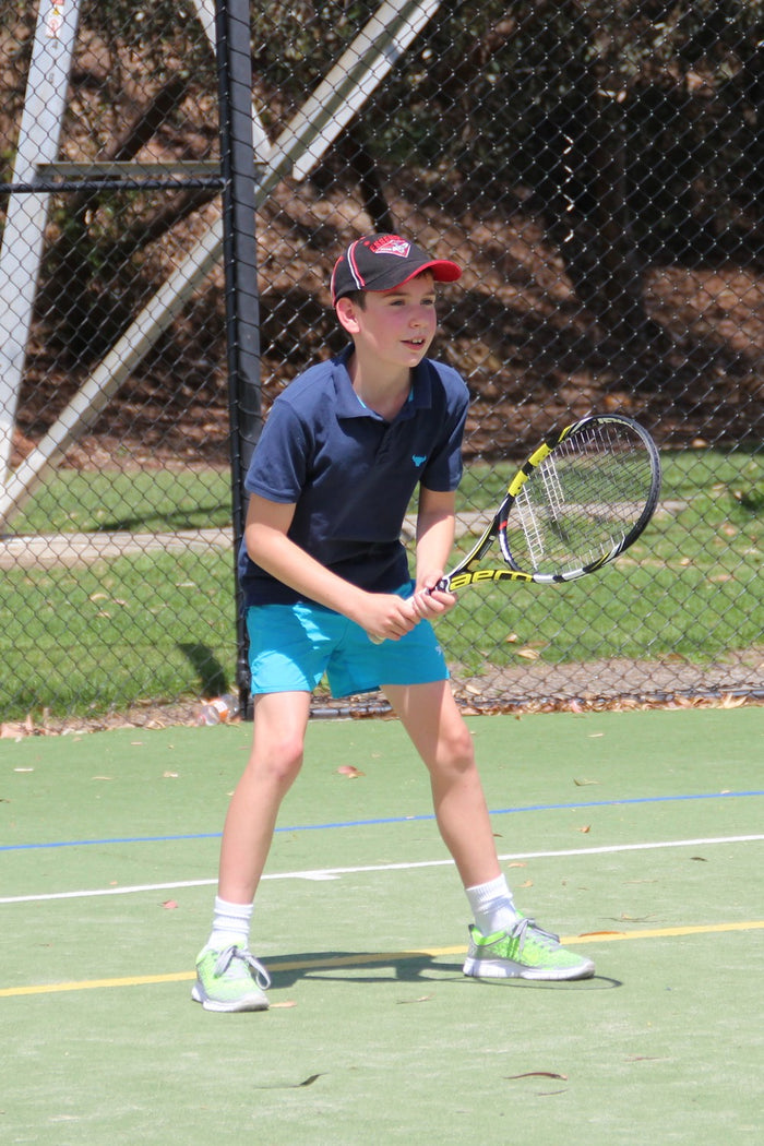 A young boy waiting to receive serve at an ASC tennis camp