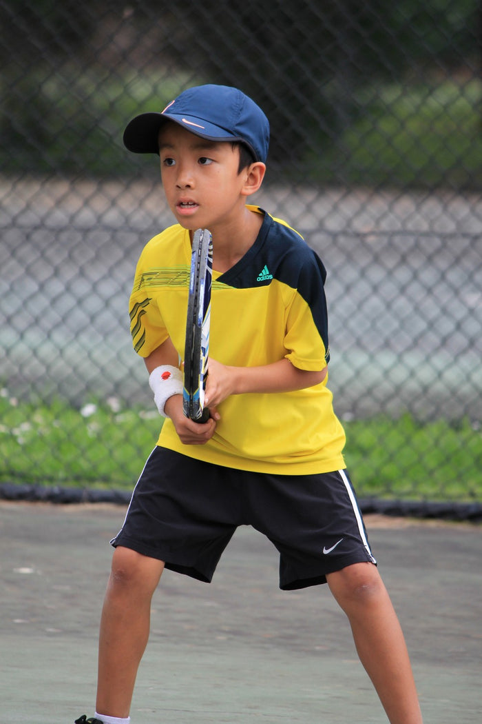 A young boy playing tennis on an outdoor court at an ASC tennis camp